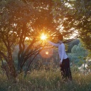 Eine Frau meditiert in der Natur, sie greift mit der Hand nach einem Sonnenstrahl in einem Baum.