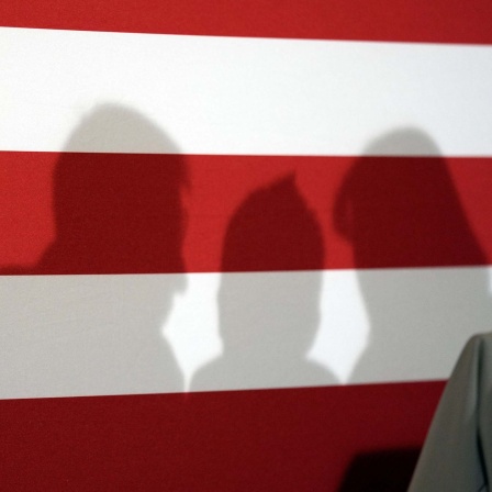 Symbolbild: drei menschliche Schatten auf einer US-Flagge.