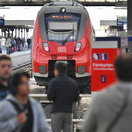 An einem Bahnhof stehen viele Menschen am Gleis und warten auf den Zug.