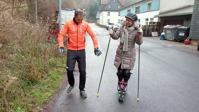 Ein Mann erklärt einer Frau das Laufen auf Ski mit Rollen.