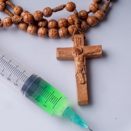 Eine Spritze liegt neben einer Kette mit einem Kreuz. (Symbolfoto)