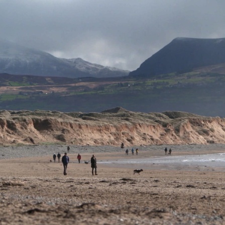 Menschen spazieren am wolkenverhagenen Strand von Wales