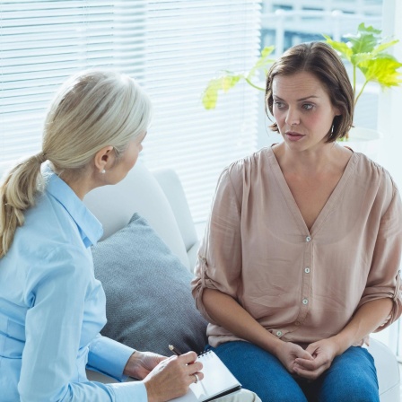 Eine junge Frau spricht zu ihrer Therapeutin, die sich Notizen macht: Studien zeigen: Von den jährlich rund 18 Millionen psychisch kranken Erwachsenen in Deutschland sucht etwa jede fünfte Person professionelle Hilfe auf.