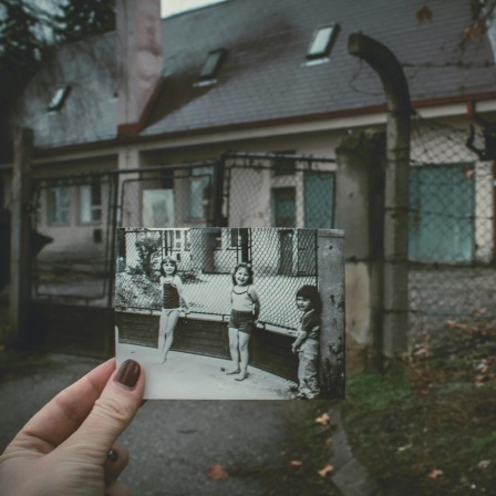 Ein Abgleich mit der Vergangenheit: Eine Frau hält an einem einsamen Schauplatz ein Schwarz-Weiß-Foto mit drei Kindern hoch - aufgenommen exakt an diesem Ort.