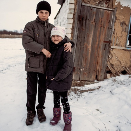 Zwei Kinder Arm in Arm vor einer Hütte im Schnee