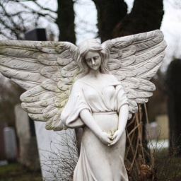 Eine Engelsfigur als Grabstein steht auf einem Friedhof.