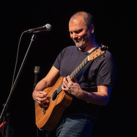 Danko Rabrenović performt mit Gitarre und Mikrofon auf einer Bühne.