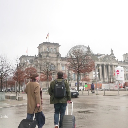Zwei Personen mit Koffern laufen zum Bundestag.