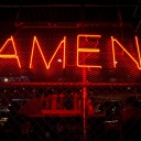 In großen roten Neonbuchstaben hängt das Wort "Amen" an einem Drahtzaun.