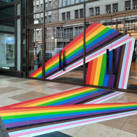 Die Fassade und der Gehweg von einem Gebäude sind mit Regenbogentape beklebt.