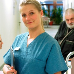 Eine Krankenschwester in selbstbewusster Haltung vor Patienten im Krankenhaus