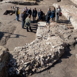 Eine kleine Gruppe Menschen steht auf den ausgegrabenen Mauerresten einer großen Kirche in der Sonne.