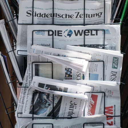 Verschiedene Tageszeitungen werden an einem Kiosk-Ständer zum Verkauf angeboten. 