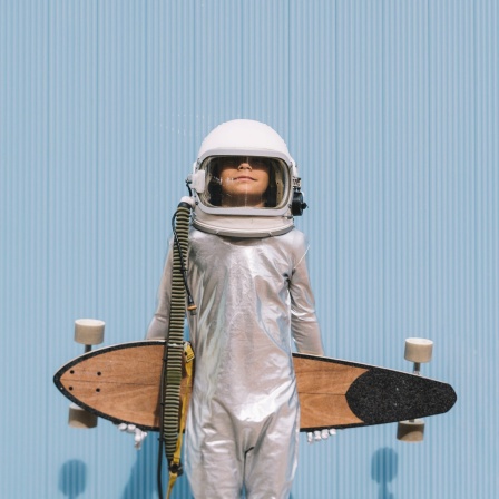 Ein Junge in Astronauten-Kostüm hält ein Longboard in den Armen.