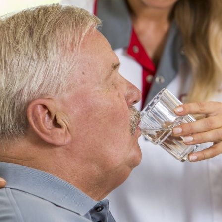 Eine Altenpflegerin hilft einem älteren Mann beim Trinken