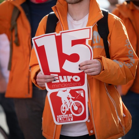 Ein Fahrer hält während eines Streiks von Fahrern des Lieferdienstes Lieferando, den die Gewerkschaft Nahrung-Genuss-Gaststätten organisiert hat, vor dem Lieferando Hub Frankfurt ein Schild mit der Aufschrift «15 Euro» hoch.