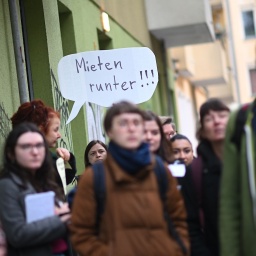 Demonstranten halten bei der Bezirkstour des Berliner Senats mit Journalisten durch Neukölln vor der Tee und Wärmestube Neukölln in der Weisestraße ein Transparent mit der Aufschrift "Mieten runter!!!" hoch.