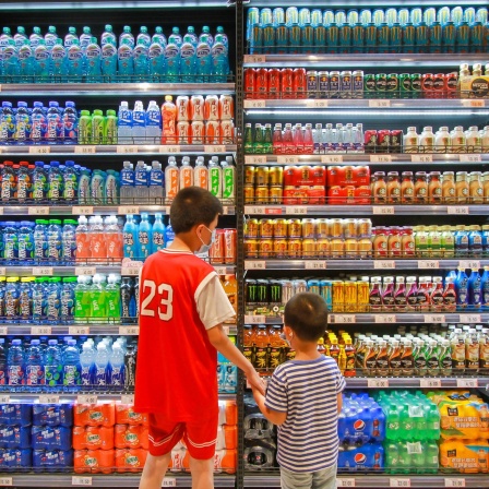 Zwei Jungs stehen in einem Supermarkt vor einem Kühlregal und suchen sich Getränke aus.