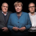 Angela Merkel steht im Vordergrund und schaut in die Kamera. Links hinter hier Prof. Dr. Thomas Fischer, rechts Holger Schmidt