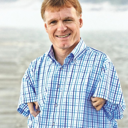 Der Hornist, Behindertensportler und Jurist Matthias Berg blickt freundlich in die Kamera. Er hat rötlich-blonde Haare und trägt ein blauweiß-kariertes Hemd.