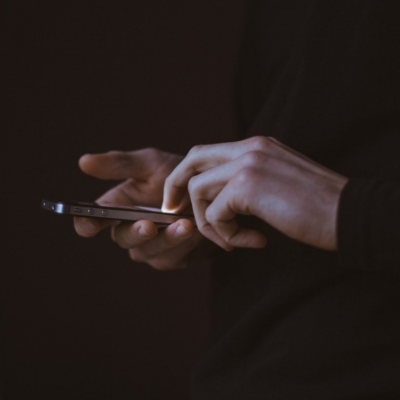 Eine Person mit Smartphone berührt dessen Touchscreen.