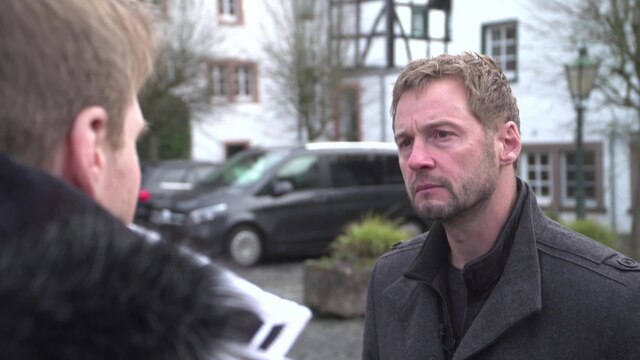 Dieter Könnes unterhält sich mit einem Mann vor einem weißen Fachwerkhaus