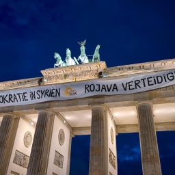 Aktivisten entrollen auf dem Brandenburger Tor ein Transparent mit der Aufschrift Â«Für Demokratie in Syrien - Rojava verteidigenÂ» als Symbol der Solidarität mit den kurdischen Gebieten in Syrien.