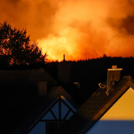 Flammen steigen hinter Häusern am Horizont auf.