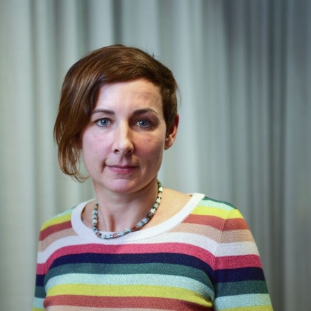 Porträtbild der Schriftstellerin Juli Zeh vor einem hellgrauen Vorhang, der Falten wirft.