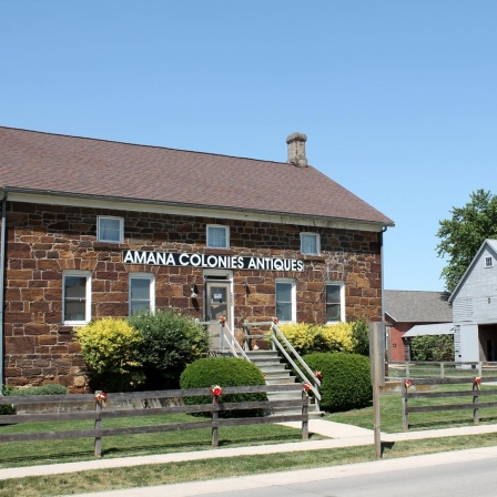 Frontansicht eine Hauses in den Amana Kolonien in Iowa. An dem gemauerten Steinhaus steht "Amana Colonies Antiques".