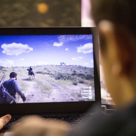 Eine Person sitzt an einem Computer und spielt Red Dead Redemption. Auf dem Bildschirm wird eine Szene aus dem Spiel dargestellt.