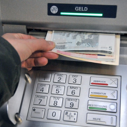 Eine Hand entnimmt dem Geldschlitz eines Bankautomaten Bargeld (Symbolbild)
