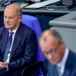 Olaf Scholz betrachtet Friedrich Merz am Rednerpult.