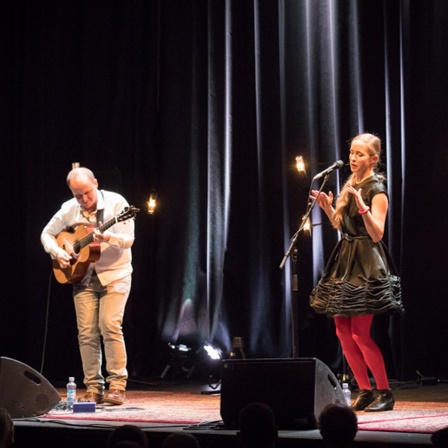 Der Gitarrist Balint Gyémánt und die Sängerin Veronica Harcsa stehen auf einer Bühne und spielen Musik.