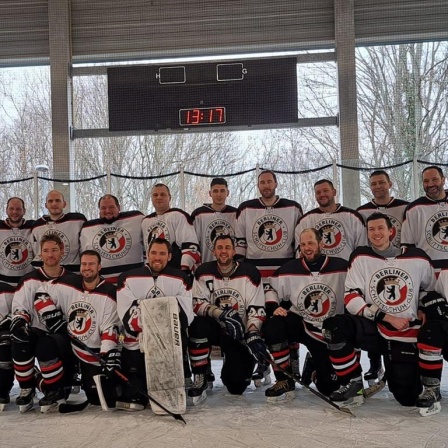 17 Eishockeyspieler posieren auf dem Eis in zwei Reihen für das Mannschaftsfoto. Auf der Brust tragen sie das runde Wappen des Berliner Schlittschuh-Clubs.