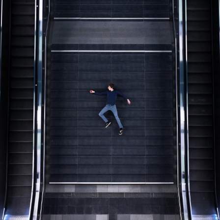 Vogelperspektive auf einen Mann, der zwischen zwei Rolltreppen auf der Treppe liegt.