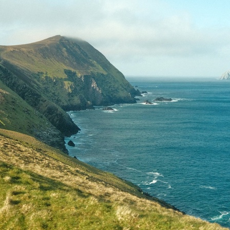 Ein Stück Küste von Irland, beschienen von der Sonne, voller schroffer Felsen, blauem Meer, und weißen Wolken