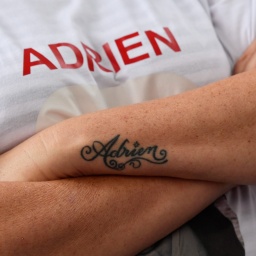 Auf den Arm eines Mannes ist der Name "Adrien" tätowiert