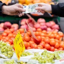 Ein Kunde bezahlt seinen Einkauf an einem Stand auf einem Wochenmarkt mit einem Fünf-Euro-Schein