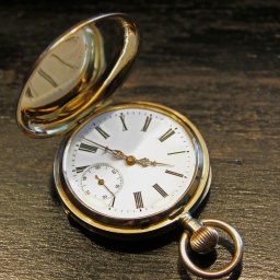 Eine aufgeklappte goldene Taschenuhr mit weißem Ziffernblatt auf einem Holztisch