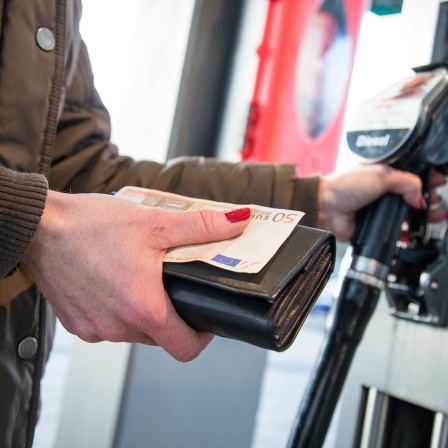 Eine Frau nimmt an einer Tankstelle in Hamburg Geld aus dem Portmonee, nachdem sie ihr Auto betankt hat