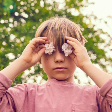 Kind hält sich Blüten vor die Augen