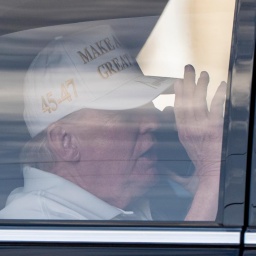 Donald Trump sitzt in einem Wagen, trägt eine weiße Baseballmütze mit dem Schriftzug "Make America Great Again" und telefoniert.