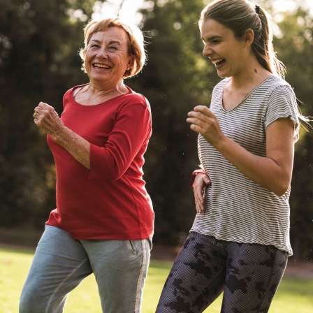 Eine ältere Frau und eine jüngere joggen zusammen im Grünen.