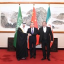 Drei Männer stehen zusammen vor den Fahnen Irans, Chinas und Saudi Arabiens. Es sind ein iranischer, ein chinesischer und ein saudi arabischer Politiker. Hinter ihnen befindet sich eine chinesische Zeichnung, das Treffen fand in China statt.