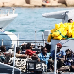 Gerettete Migranten sitzen auf einem Boot der italienischen Finanzpolizei, bevor sie im Hafen der sizilianischen Insel Lampedusa von Bord gehen (Bild: picture alliance / Cecilia Fabiano)