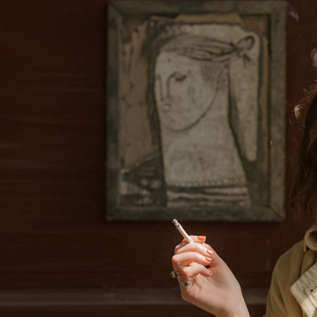 Eine junge Frau raucht vor einem gemalten Frauenporträt.
