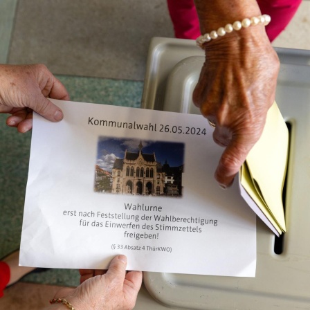 Eine Frau steckt ihre Wahlzettel in die Wahlurne.