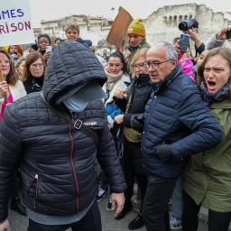 Ein maskierter Angeklagter im Vergewaltigungsprozess von Avignon geht zum Gericht. Um ihn herum sind wütende Menschen zu sehen.