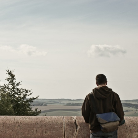 Ein Mann steht vor einer Betonbrüstung und schaut in die Landschaft.